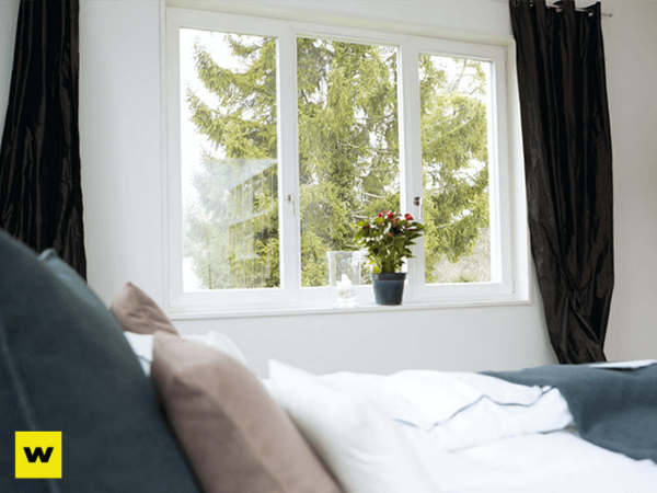 Helles Schlafzimmer mit großem Fenster, Zimmerpflanze und Ausblick ins Grüne.
