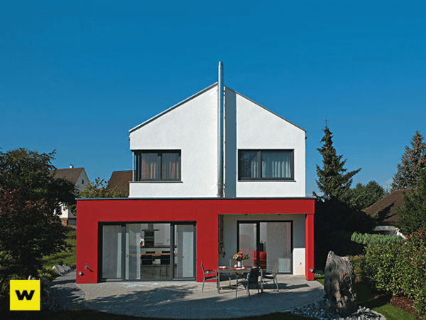 Modernes Einfamilienhaus mit Flachdach, roter Fassade und großem Garten bei Sonnenschein.