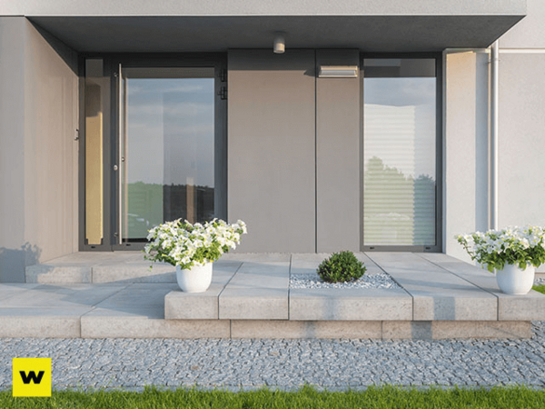 Moderner Hauseingang mit grauen Fliesen, Glasfront und Blumen in weißen Pflanzkübeln.